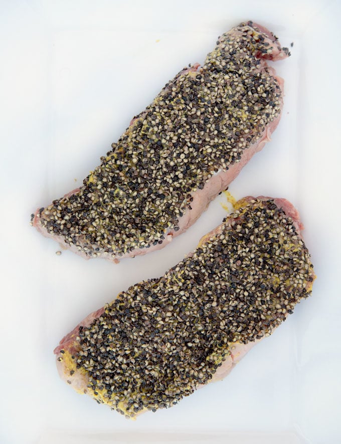 steaks coated with cracked black peppercorns on a white cutting board