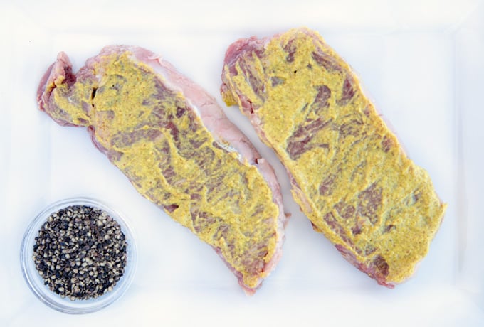 steaks coated with mustard on a white cutting board