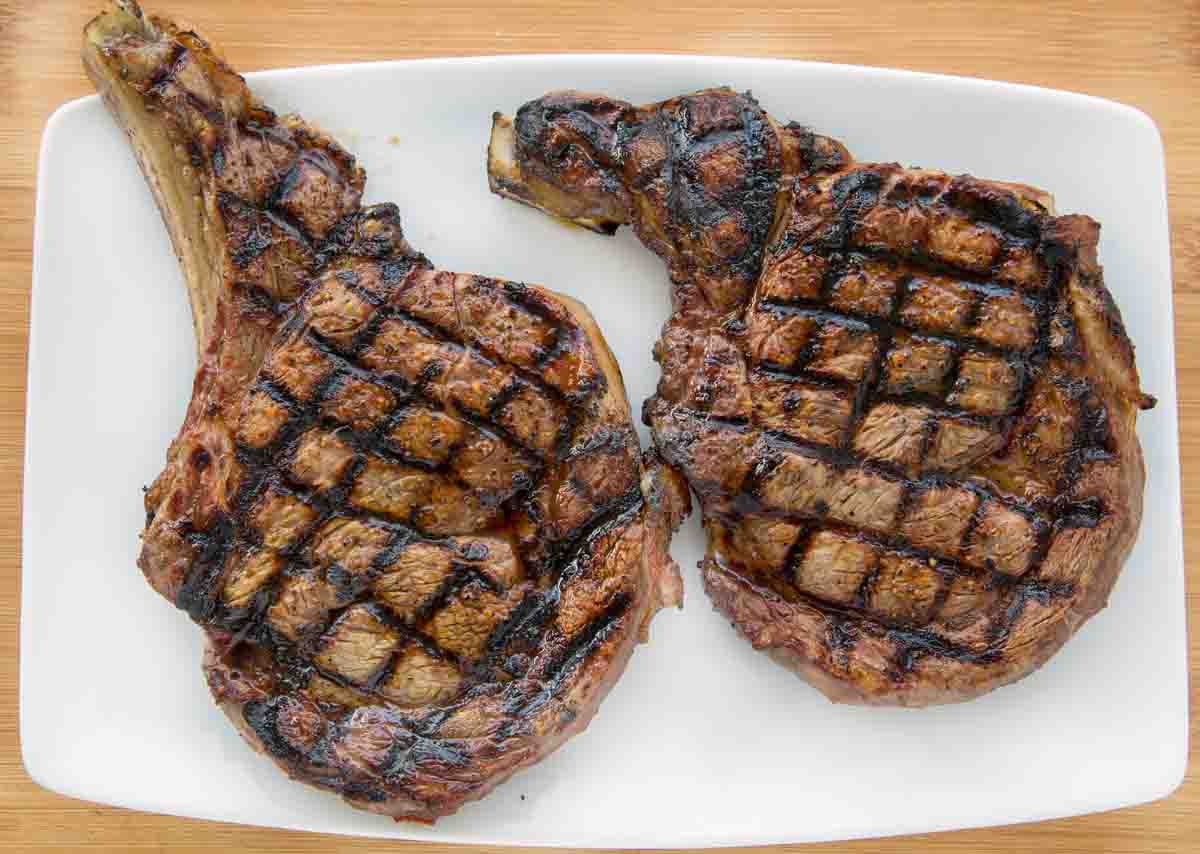 two grilled ribeyes with crosshatch marks on a white platter