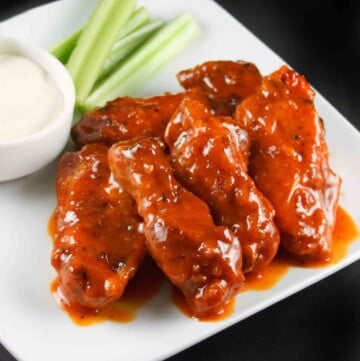 buffalo chicken wings with celery sticks and bleu cheese dressing on a white plate