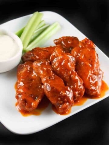 buffalo chicken wings with celery sticks and bleu cheese dressing on a white plate