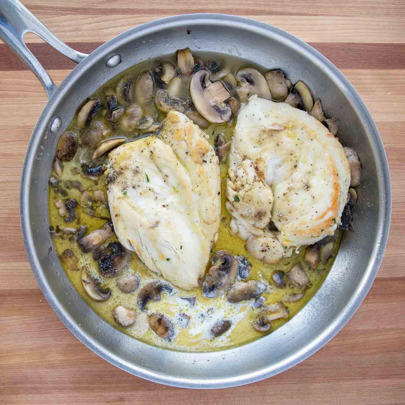 Stock and cream added to the chicken marsala in a saute pan.