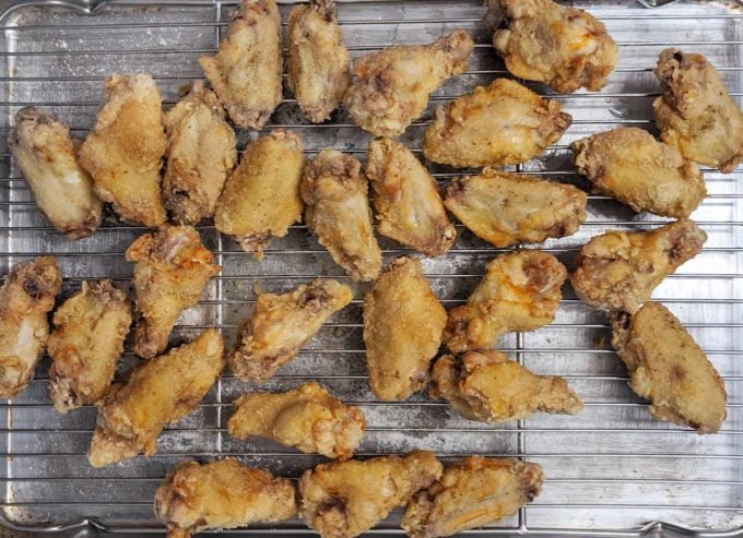 overhead view of fried chicken wings draining on a wire rack on a sheet pan
