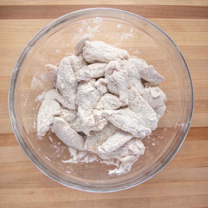 overhead view of a glass bowl with chicken wing sections coated in seasoned flour