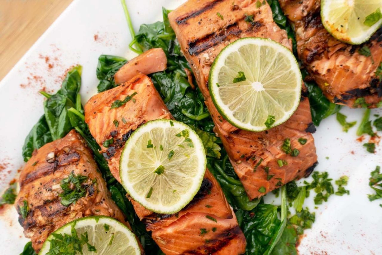 overhead view of marinated grilled salmon un a bed of spinach with slices of lime on top