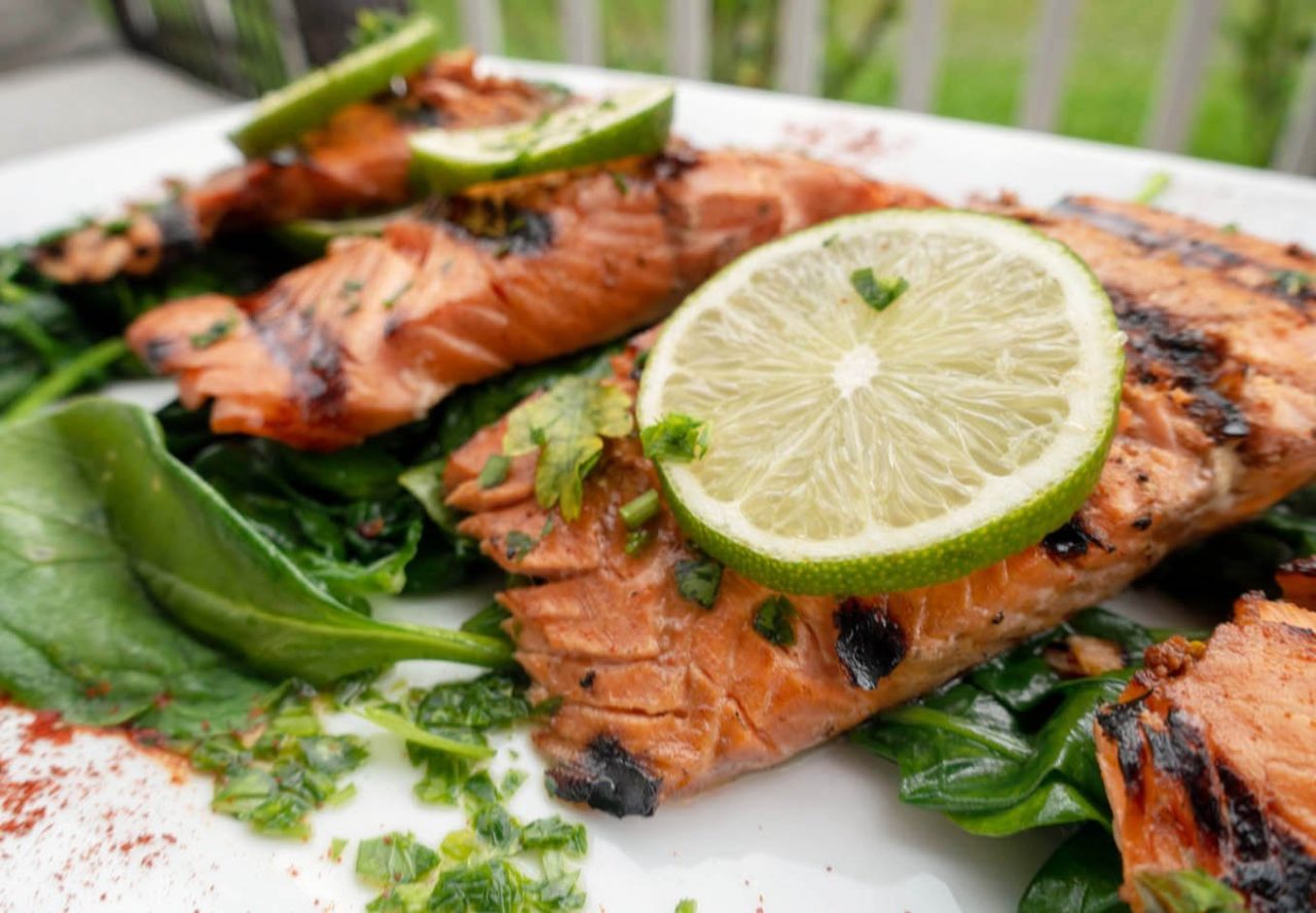 marinated grilled salmon un a bed of spinach with slices of lime on top