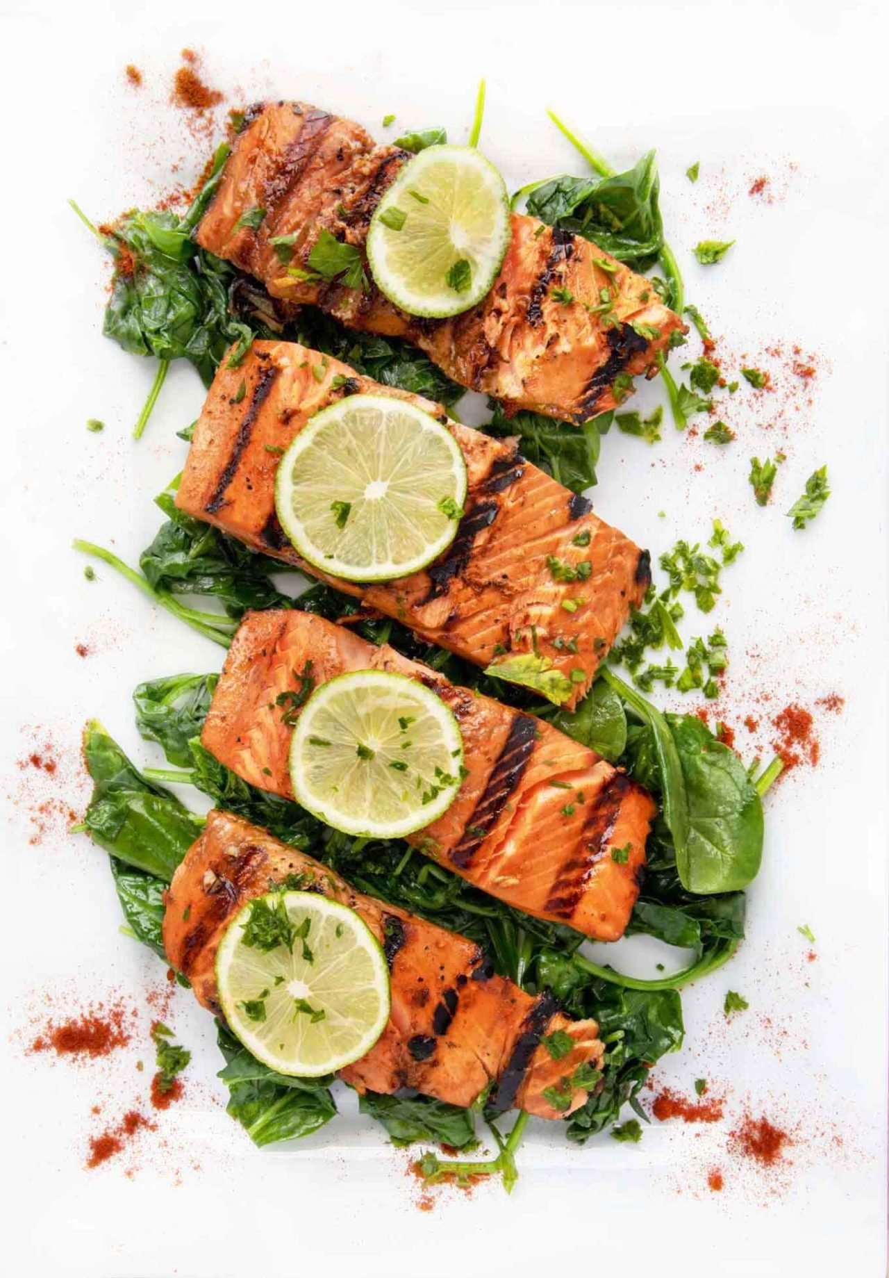 overhead view of marinated grilled salmon with lime slices on top sitting on a bed of wilted spinach on a white platter