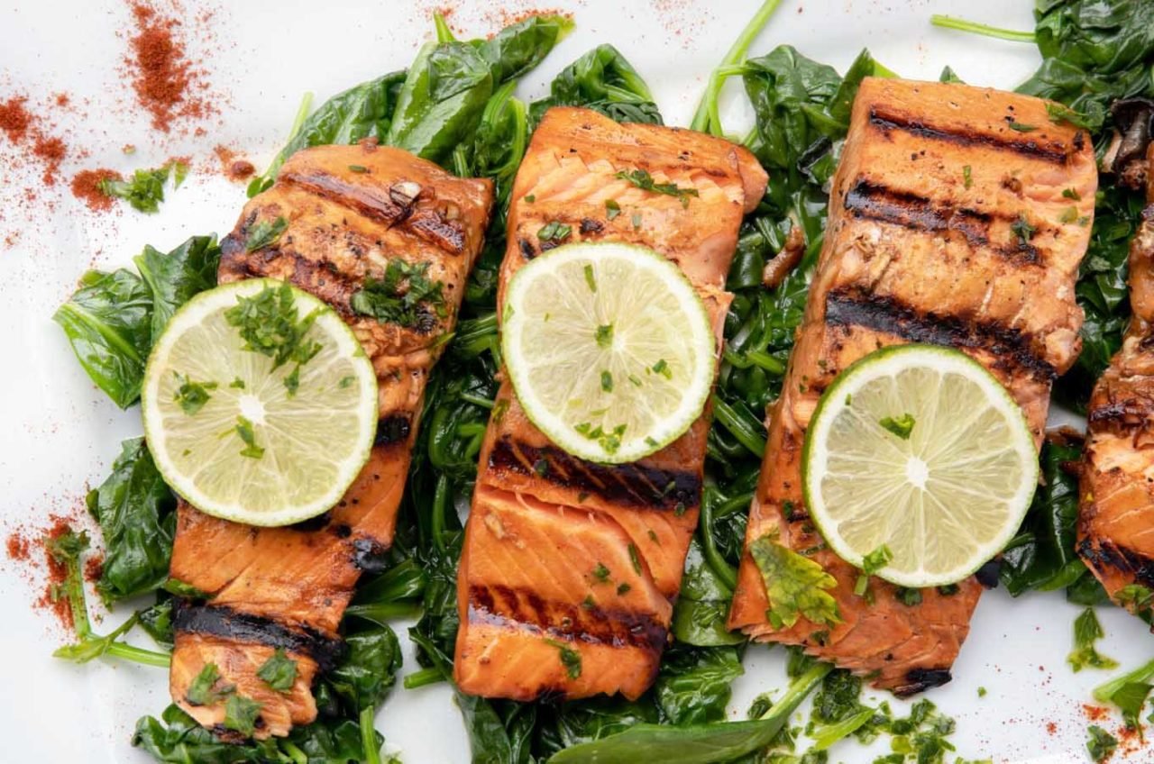 overhead view of marinated grilled salmon un a bed of spinach with slices of lime on top