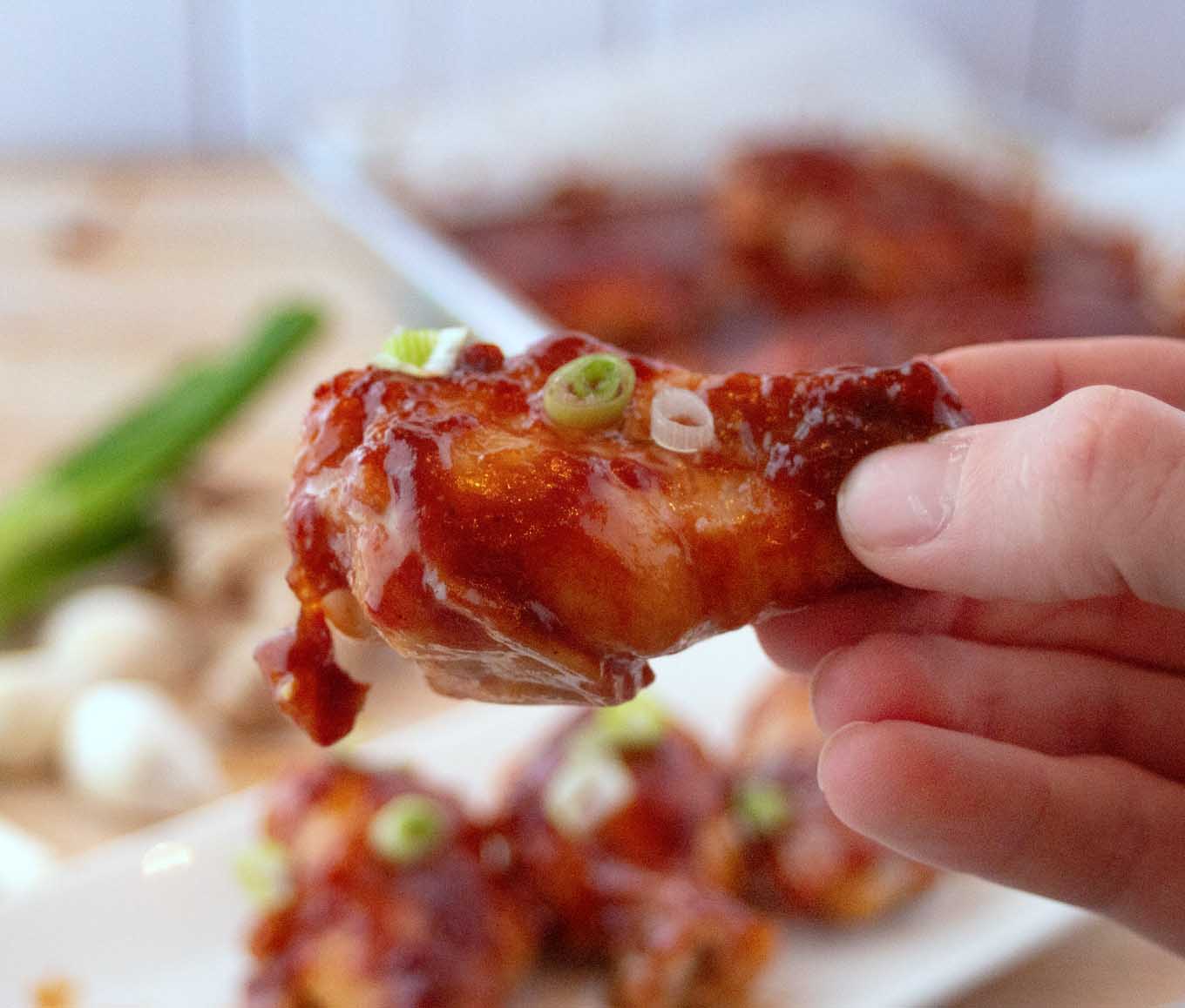 hand holding a Chinese Sticky wing with more in the background