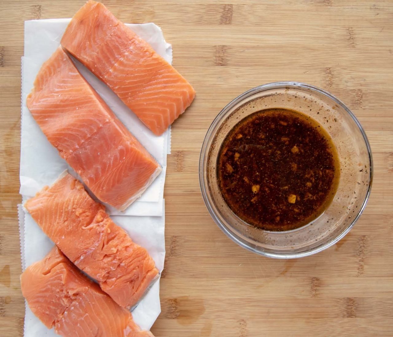 4 salmon filets on white paper next to a glass bowl of marinade 