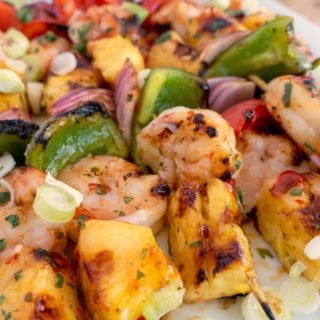 close up of grilled shrimp and pineapple skewers on white platter
