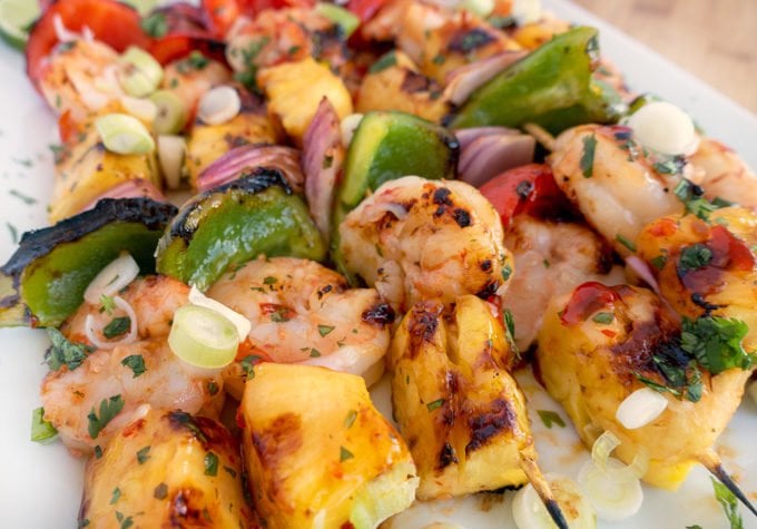 close up of grilled shrimp and pineapple skewers on white platter