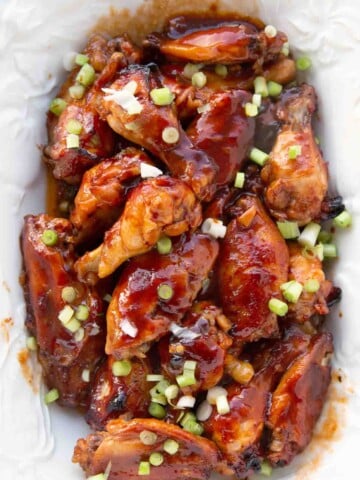 chinese sticky wings on a white platter with chopped scallion garnish