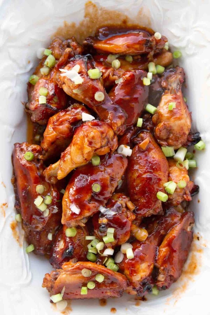 chinese sticky wings on a white platter with chopped scallion garnish
