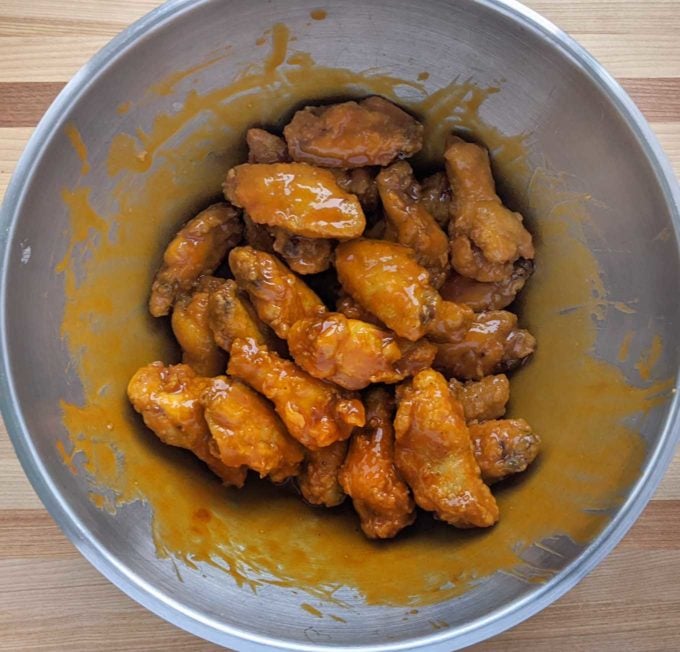 overhead view of fried chicken wings coated in buffalo sauce in a large stainless steel bowl