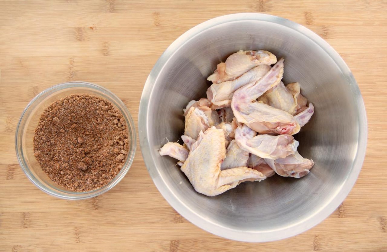glass bowl of mixed spices for dryrub and metal bowl of raw cut chicken wings.