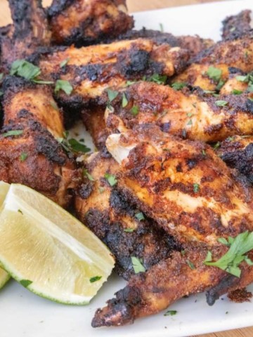 white platter of grilled and charred dry rub chicken wings with chopped parsley sprinkled on top