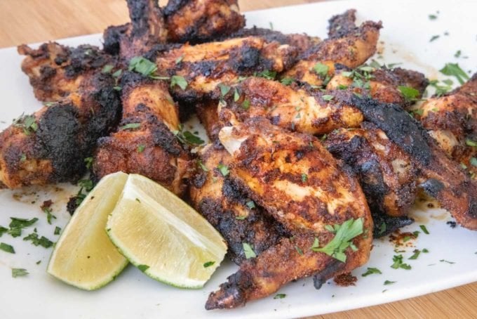 white platter of grilled and charred dry rub chicken wings with chopped parsley sprinkled on top