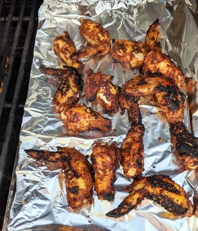 chicken wings on a tinfoil sheet on top of a grill