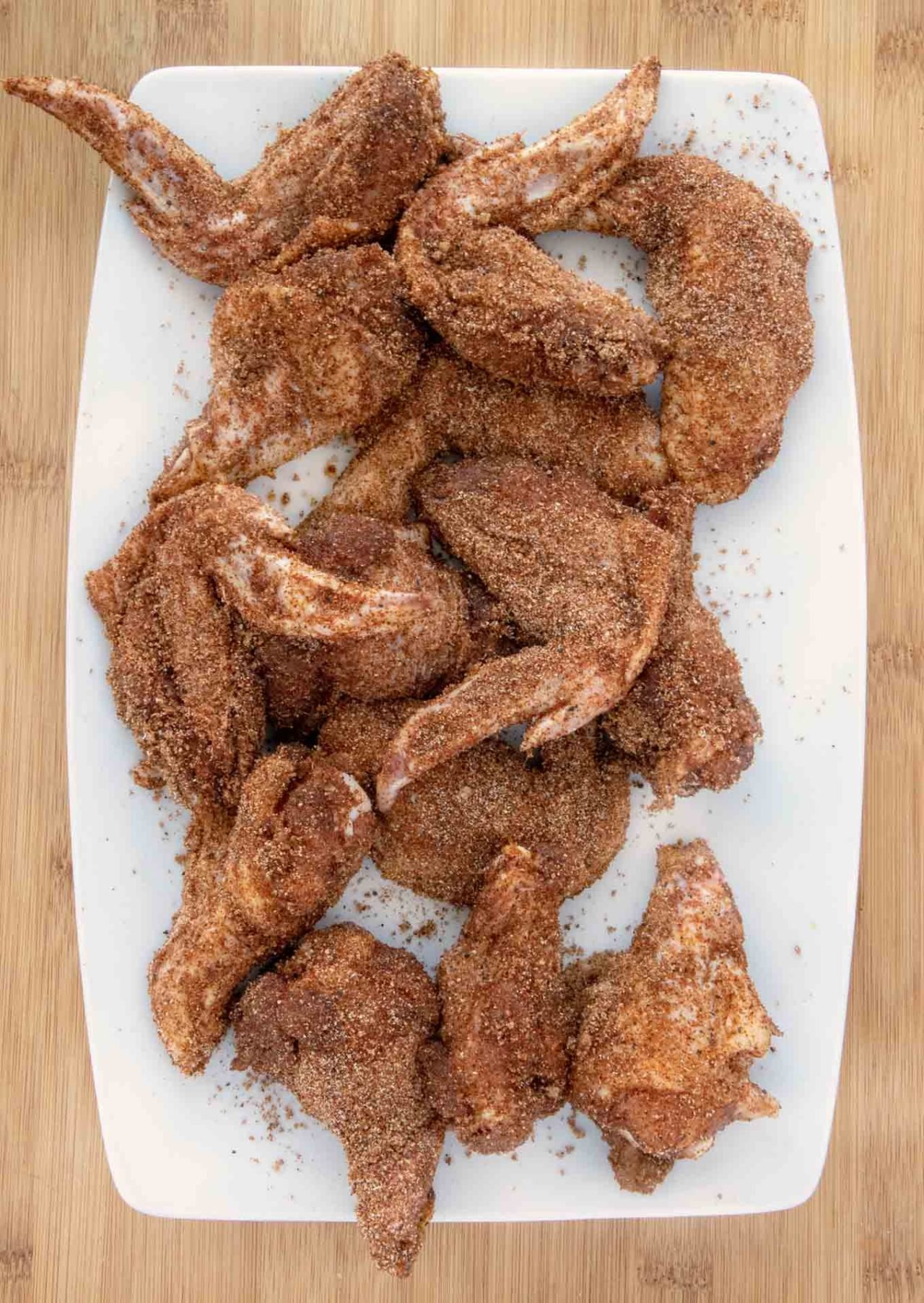 raw seasoned wings on a white platter .