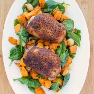 pan seared duck breast with crispy skin on a bed of veggies on a white platter