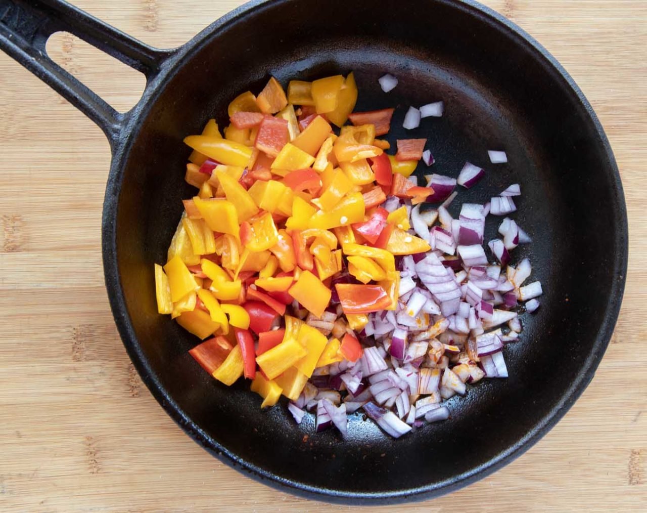 diced raw tri color peppers and diced raw red onions in a cast iron skillet