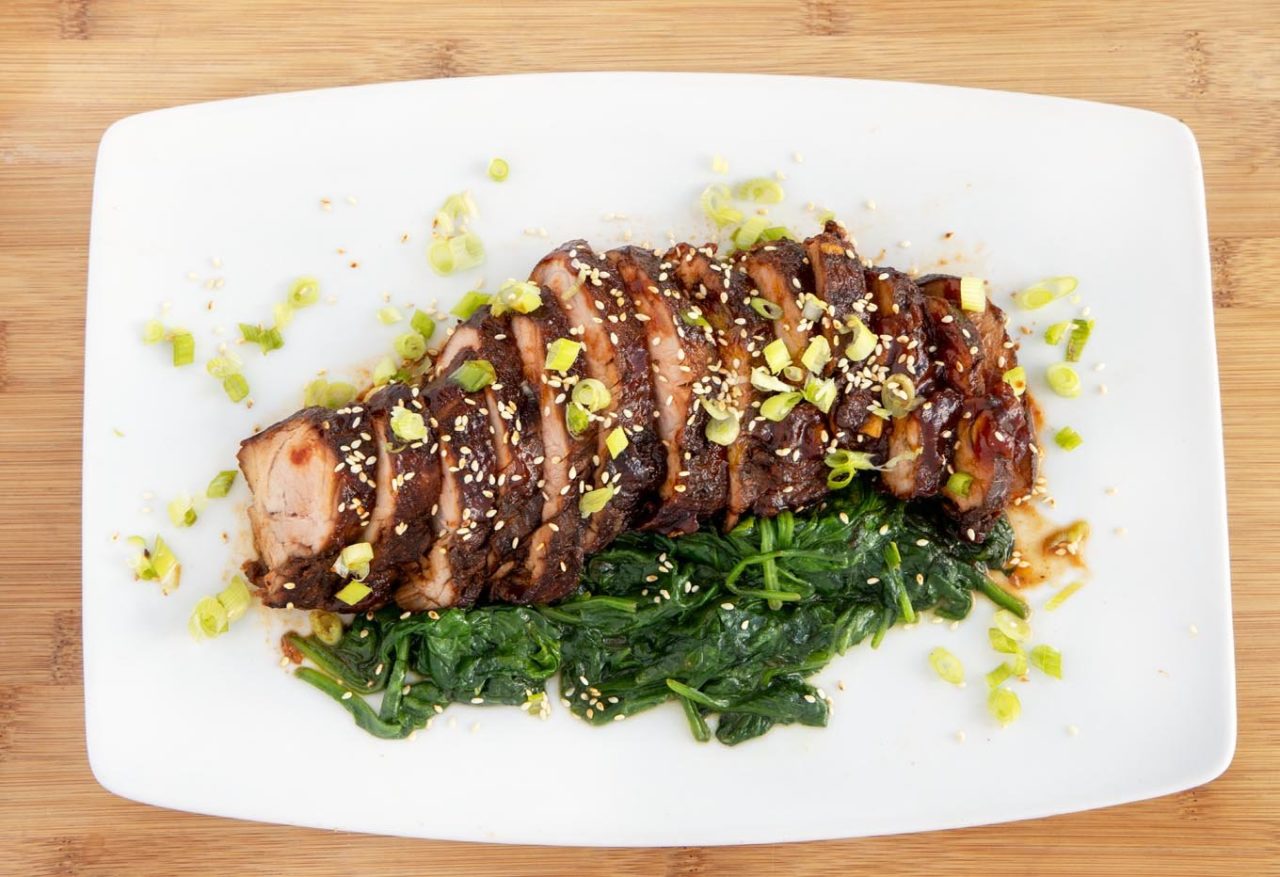 White Platter with sliced pork tenderloin and spinach.