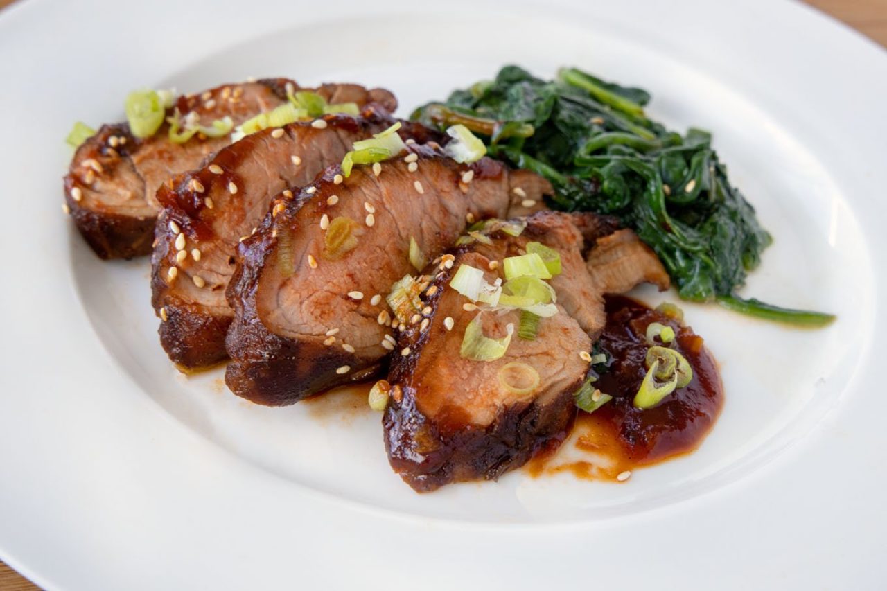 slices of Korean Pork Barbecue on a white plate sprinkled with toasted sesame seeds and sliced scallions