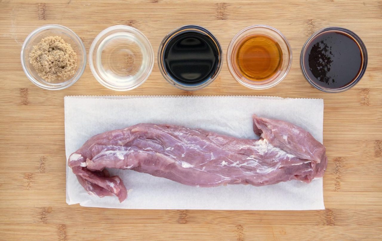 ingredients for the marinade in glass bowls and pork tenderloin on a white plate