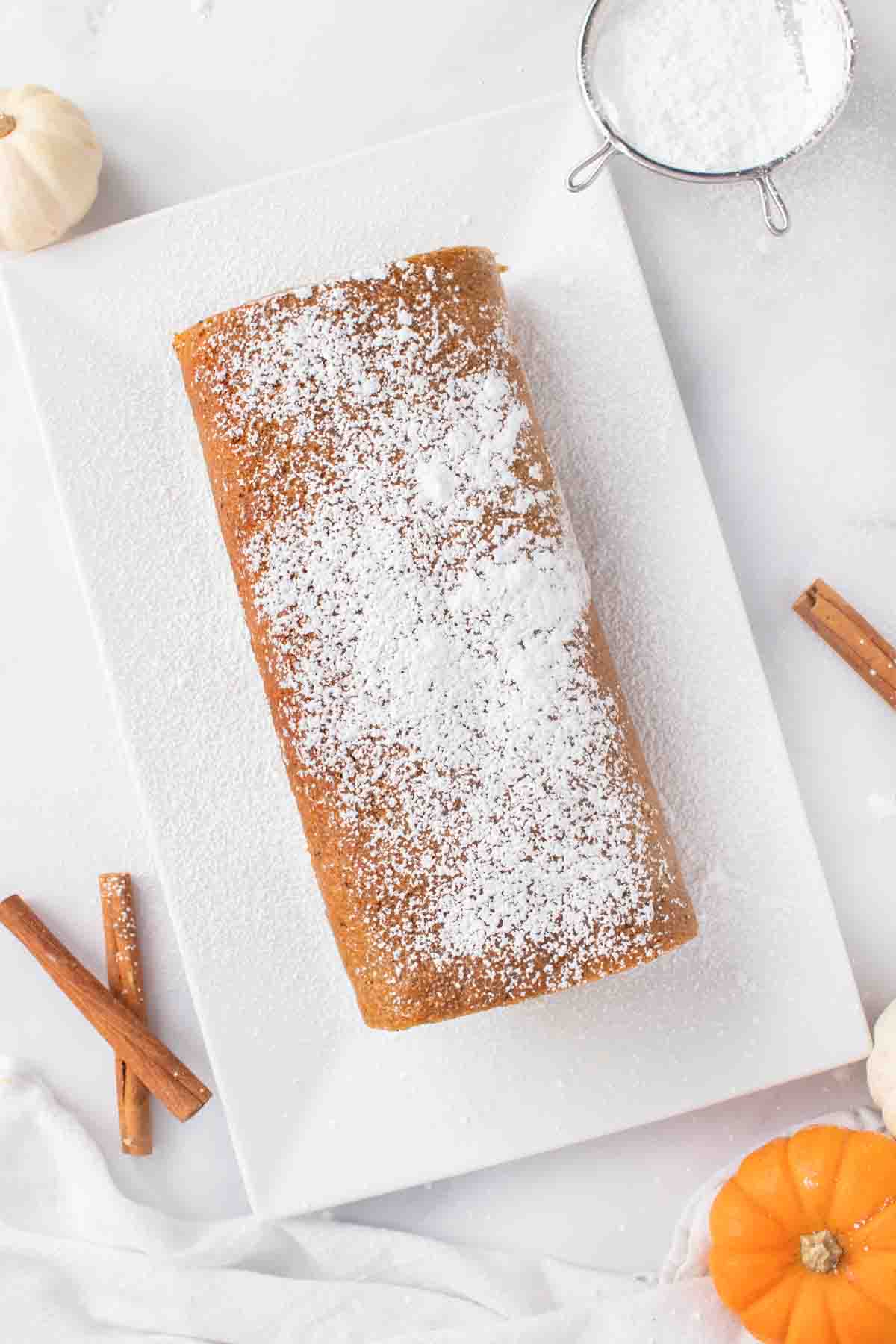 pumpkin roll on a white platter topped with powdered sugar