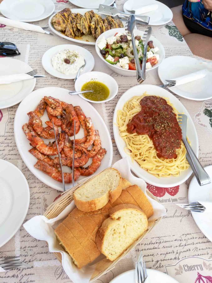 white platters of grilled shrimp, pasta with sauce and bread