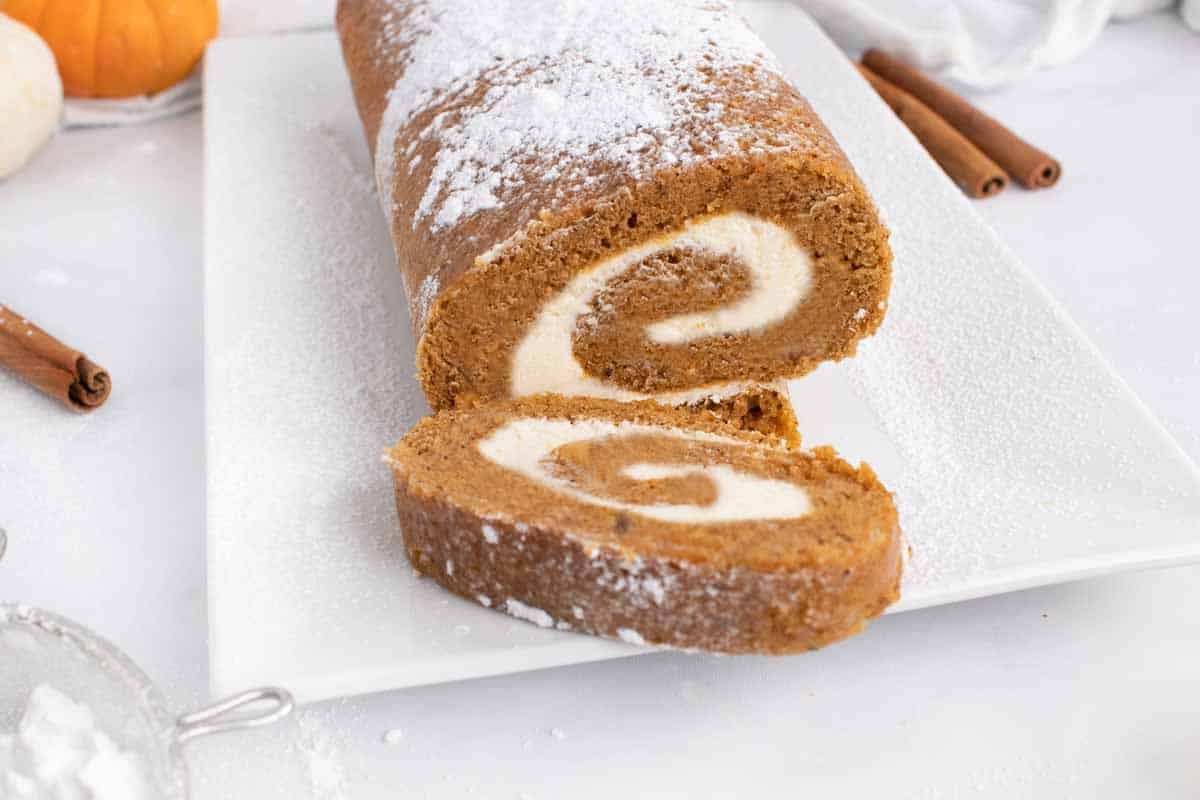 slice of pumpkin roll in front of the roll on a white platter