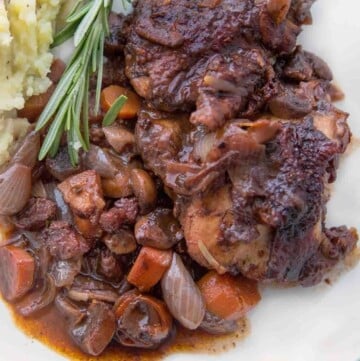 coq au vin on a white plate with mashed potatoes.