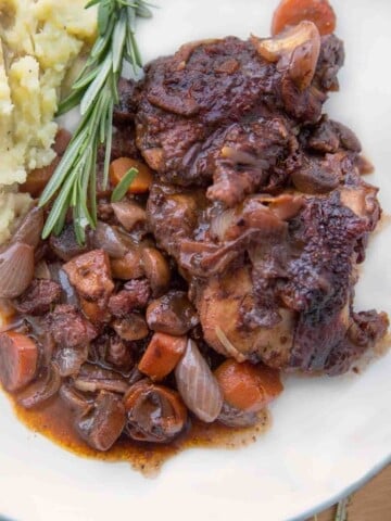 coq au vin on a white plate with mashed potatoes.
