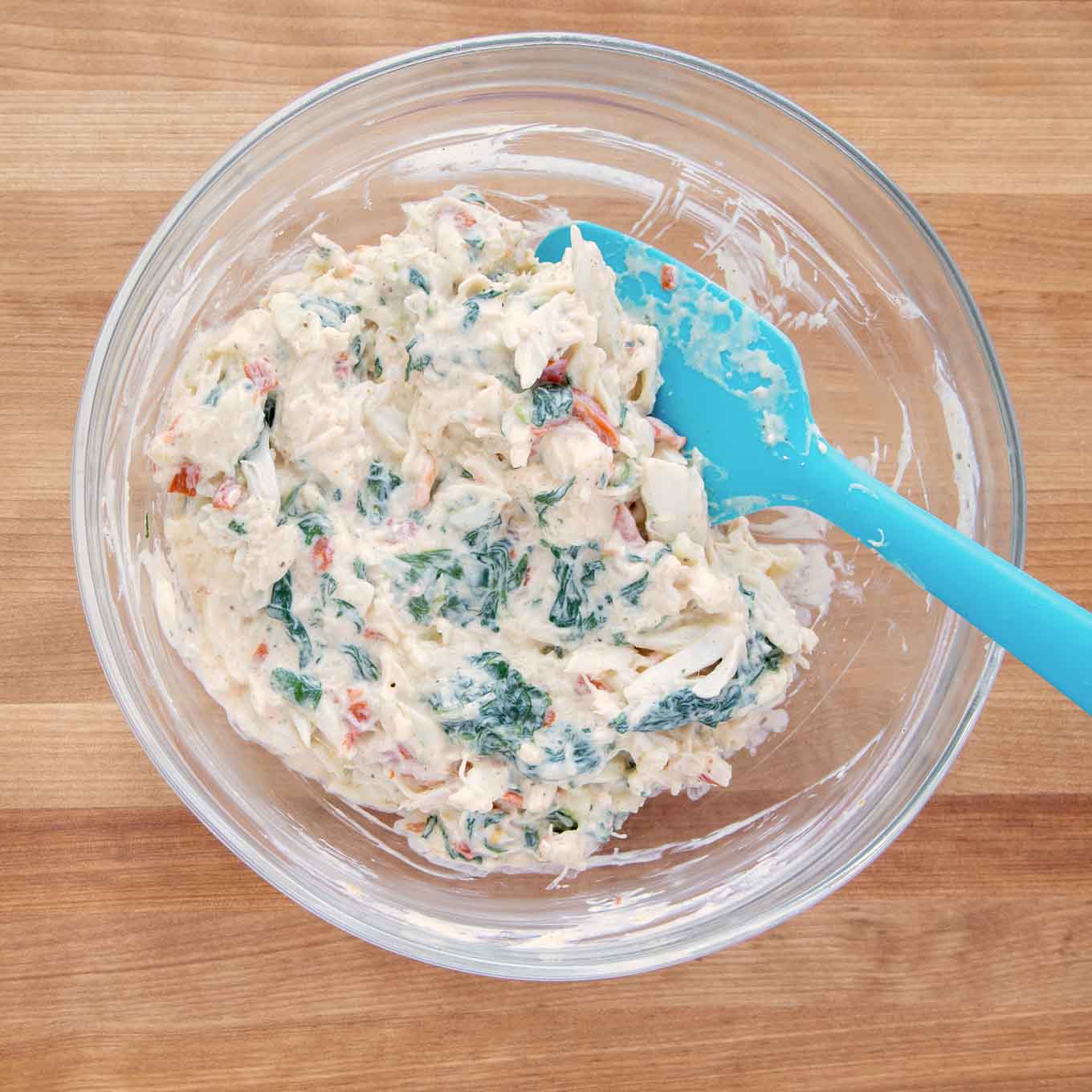 crabmeat and cheese stuffing all mixed together in a glass bowl with a blue rubber spatula 