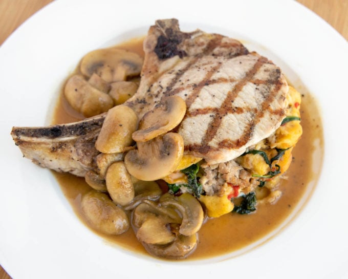 stuffed pork chop with grill marks on a white plate with mushroom gravy