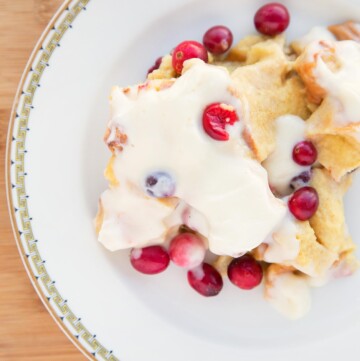 cranberry bread pudding with a cream cheese topping on a white plate with a gold rim