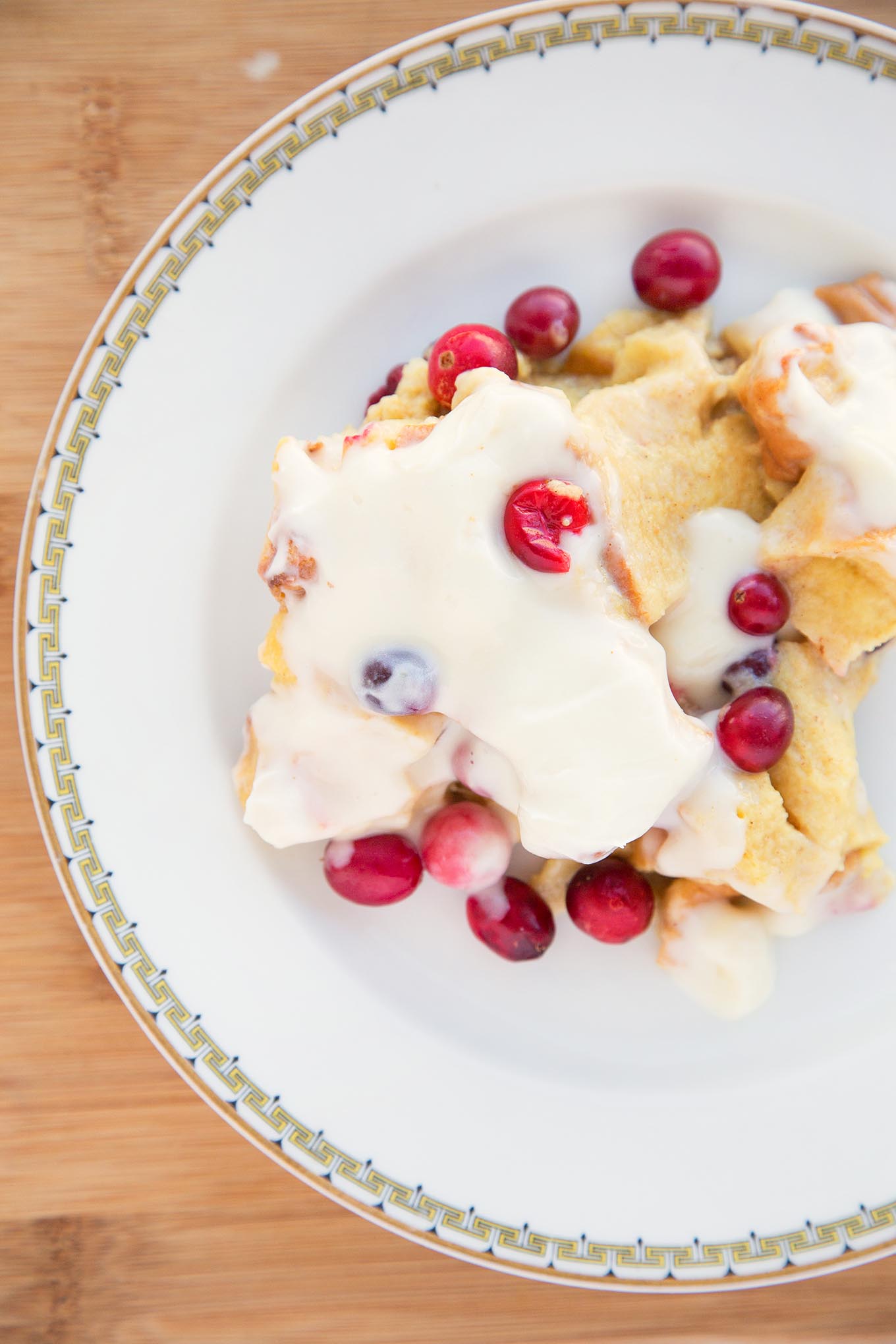 cranberry bread pudding with a cream cheese topping on a white plate with a gold rim