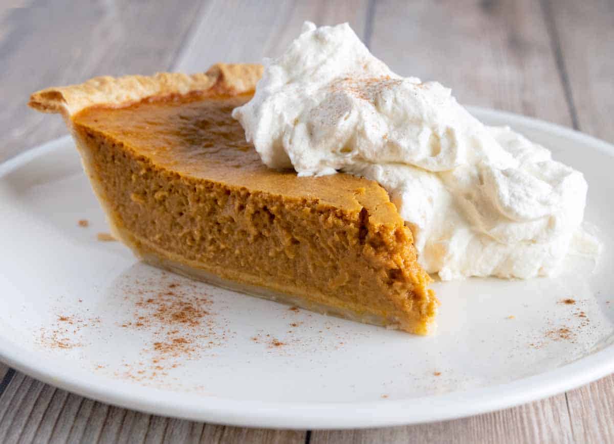 slice of creamy pumpkin pie with whipped cream on a white plate