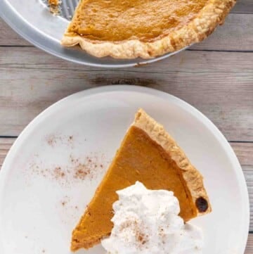 pumpkin pie with whipped cream on a white plate with reminder of pie in tin