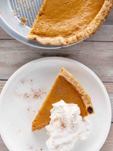 pumpkin pie with whipped cream on a white plate with reminder of pie in tin