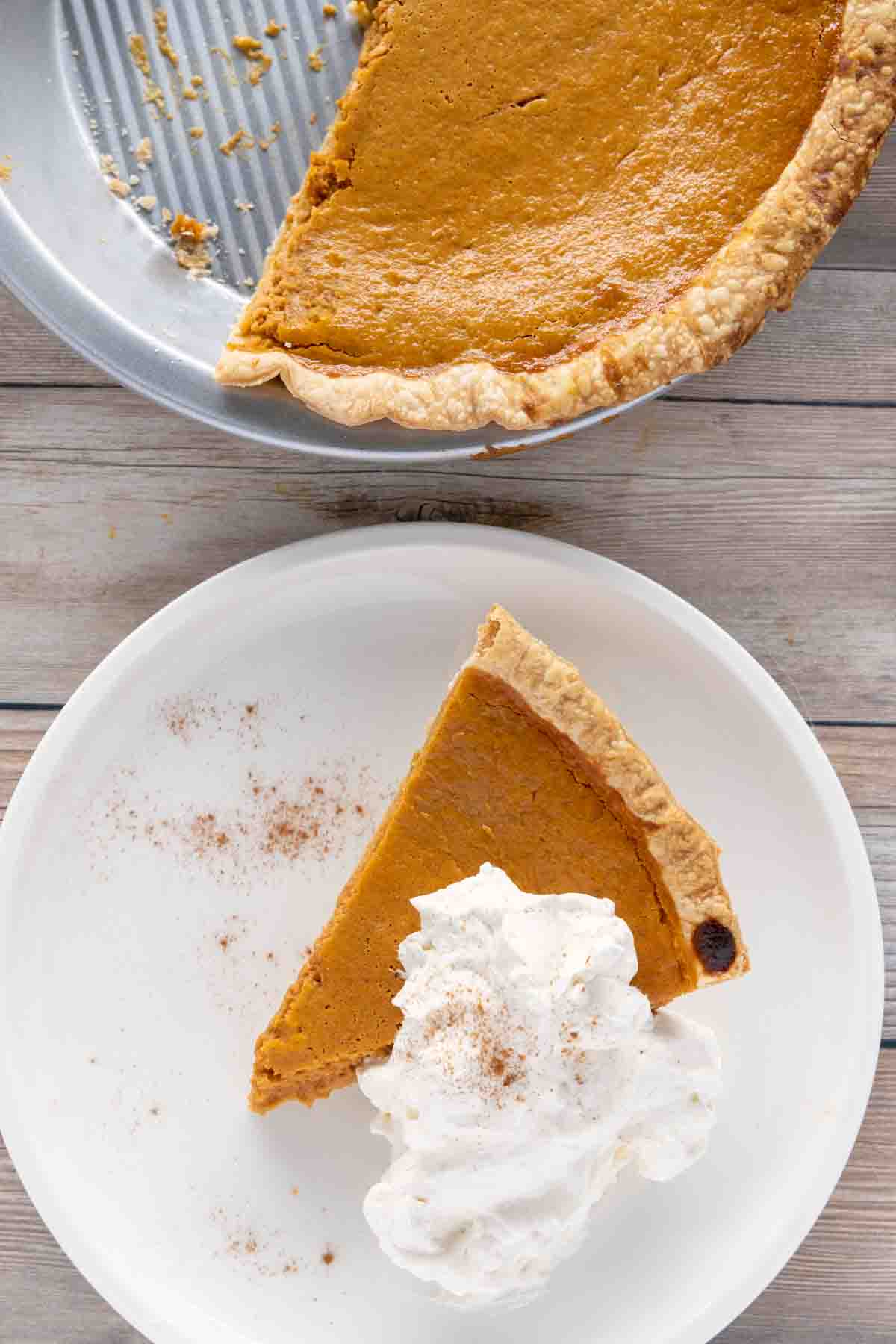 pumpkin pie with whipped cream on a white plate with reminder of pie in tin