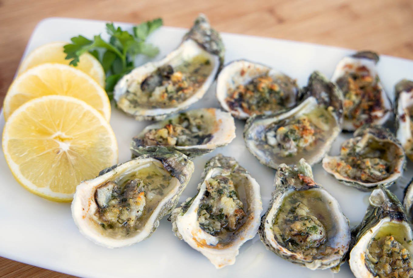 Garlic oysters on a white plate with lemon slices and parsley 