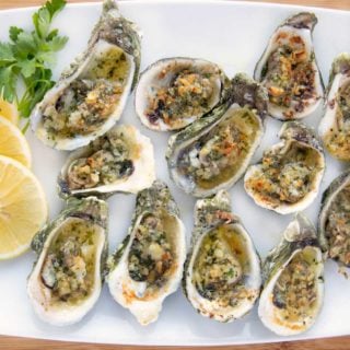 overhead shot of garlic oysters on a white platter with lemon slices and parsley