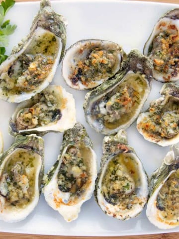 overhead shot of garlic oysters on a white platter with lemon slices and parsley