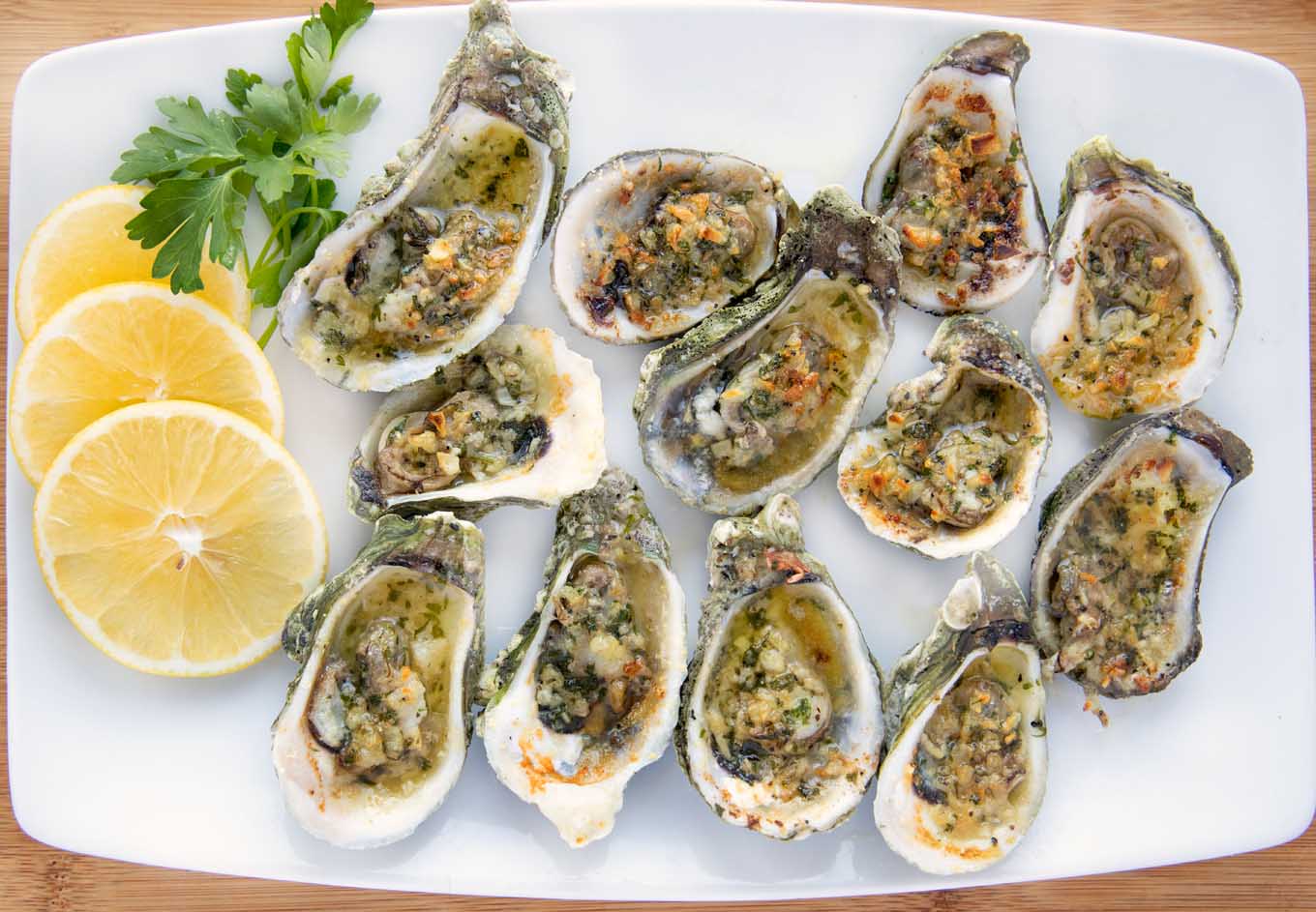 overhead shot of garlic oysters on a white platter with lemon slices and parsley