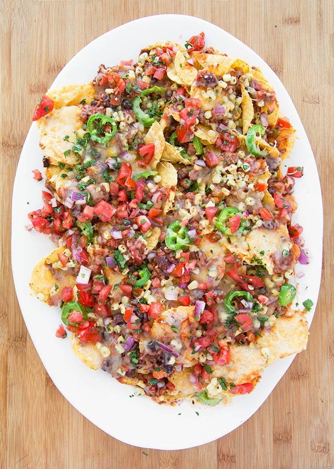 Ultimate Nachos topped with chili and beans, roasted yellow corn kernels, and sliced jalapeños topped with shredded cheddar cheese 