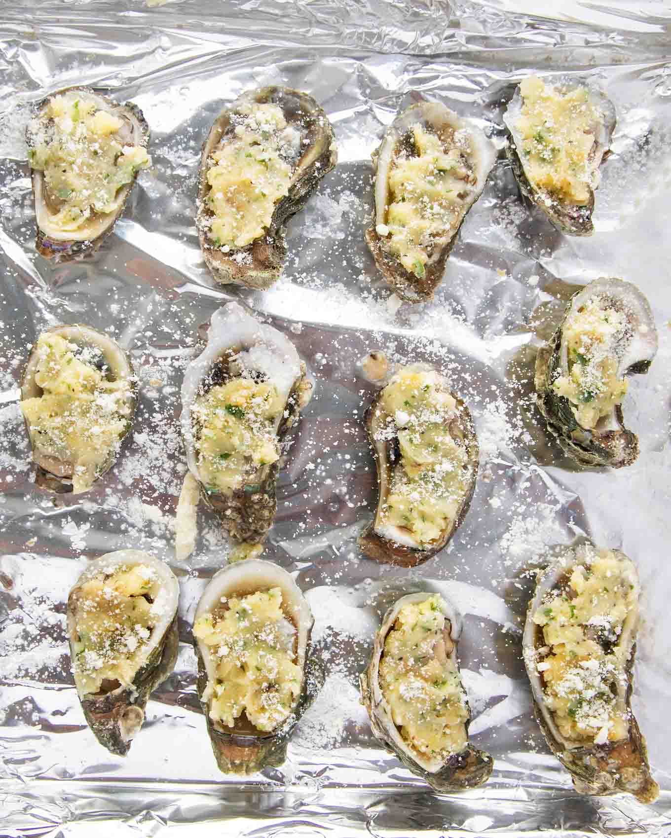 oysters topped with garlic butter and grated romano cheese on a foil lined pan