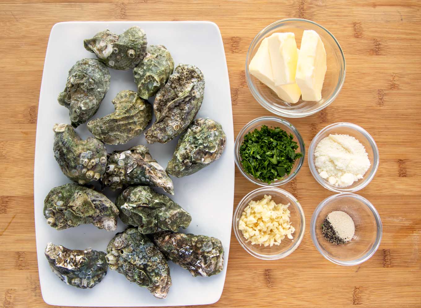 ingredients ot make garlic oysters in small glass bowls with a platter of unshucked oysters