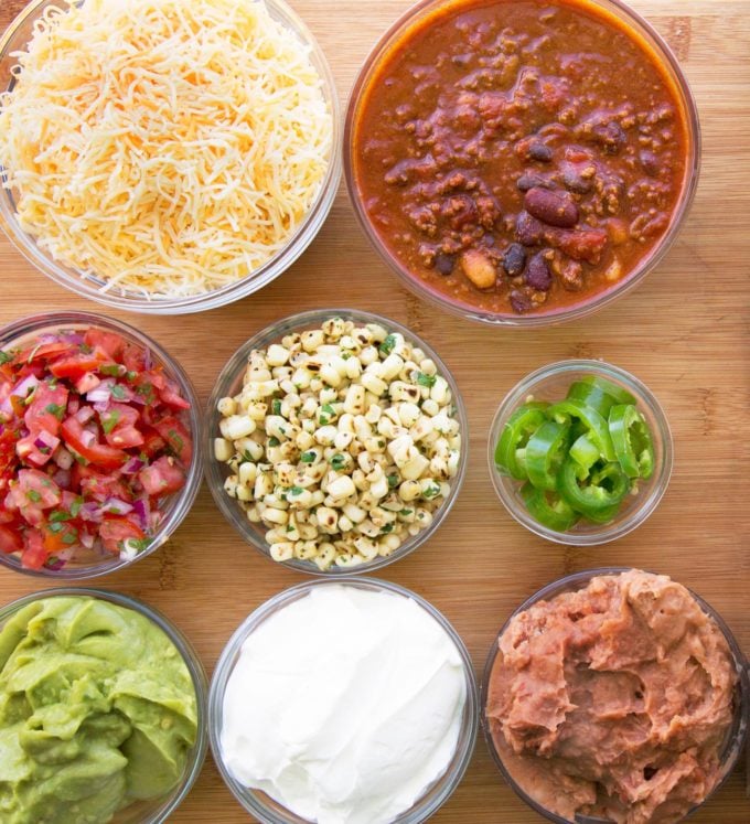 ingredients to make ultimate nachos in glass bowls on wooden cutting board